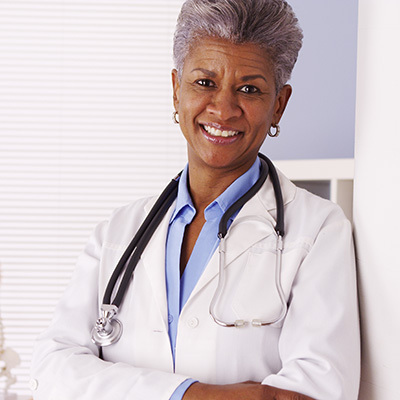 smiling doctor, wearing a stethoscope, standing against a wall and folding her arms