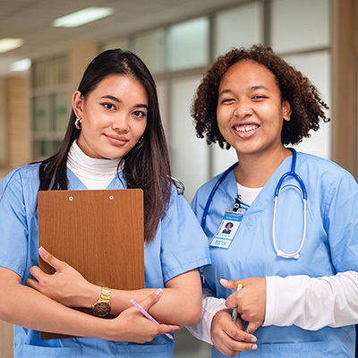 two smiling nurses wearing light blue scrubs